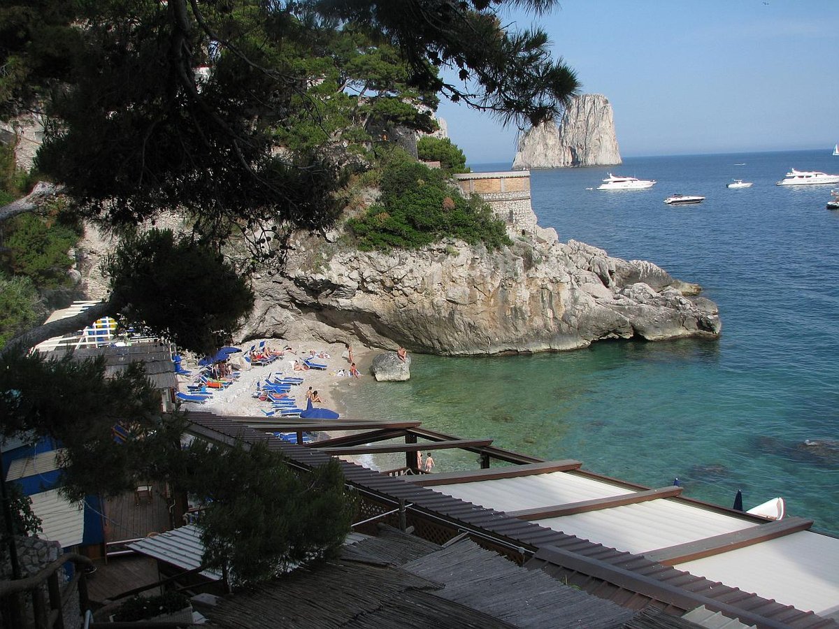 Área de playa rocosa gratuita de Marina Piccola en Capri con nadadores y rocas Faraglioni al fondo