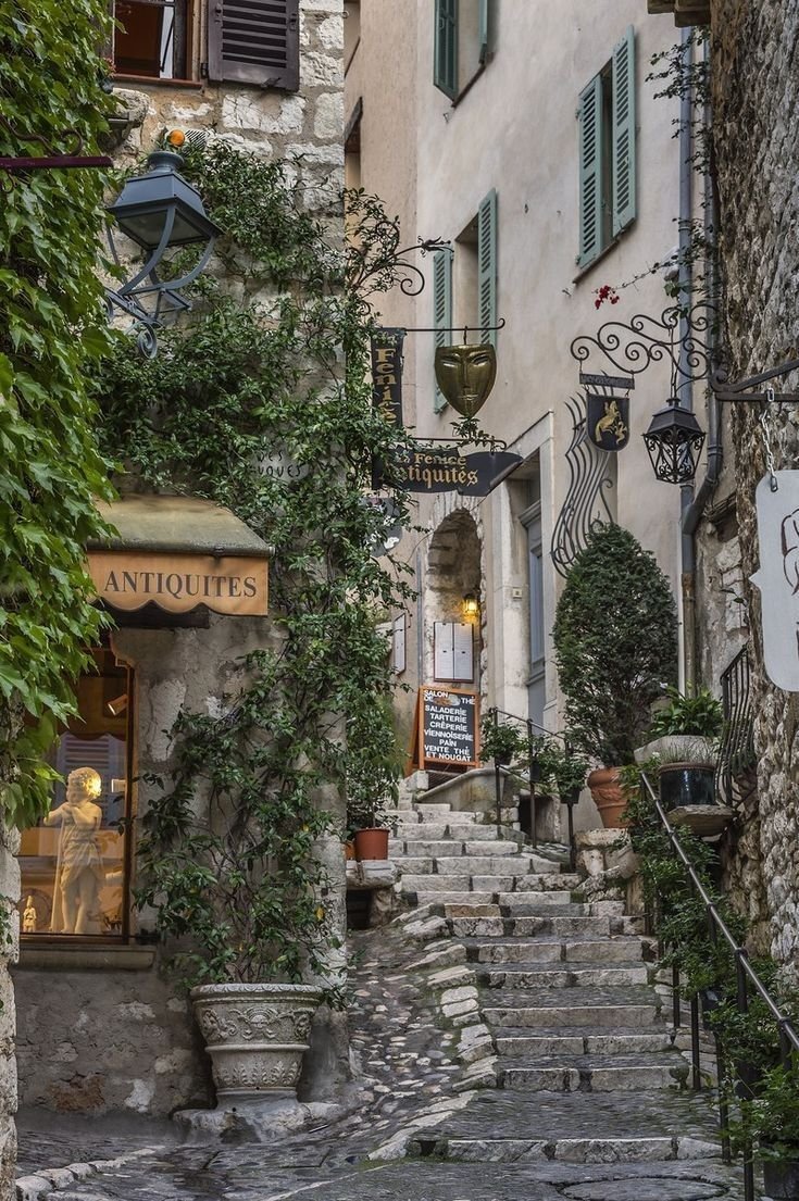 Escalones de piedra subiendo por un callejón estrecho del casco antiguo con plantas y letreros de tiendas