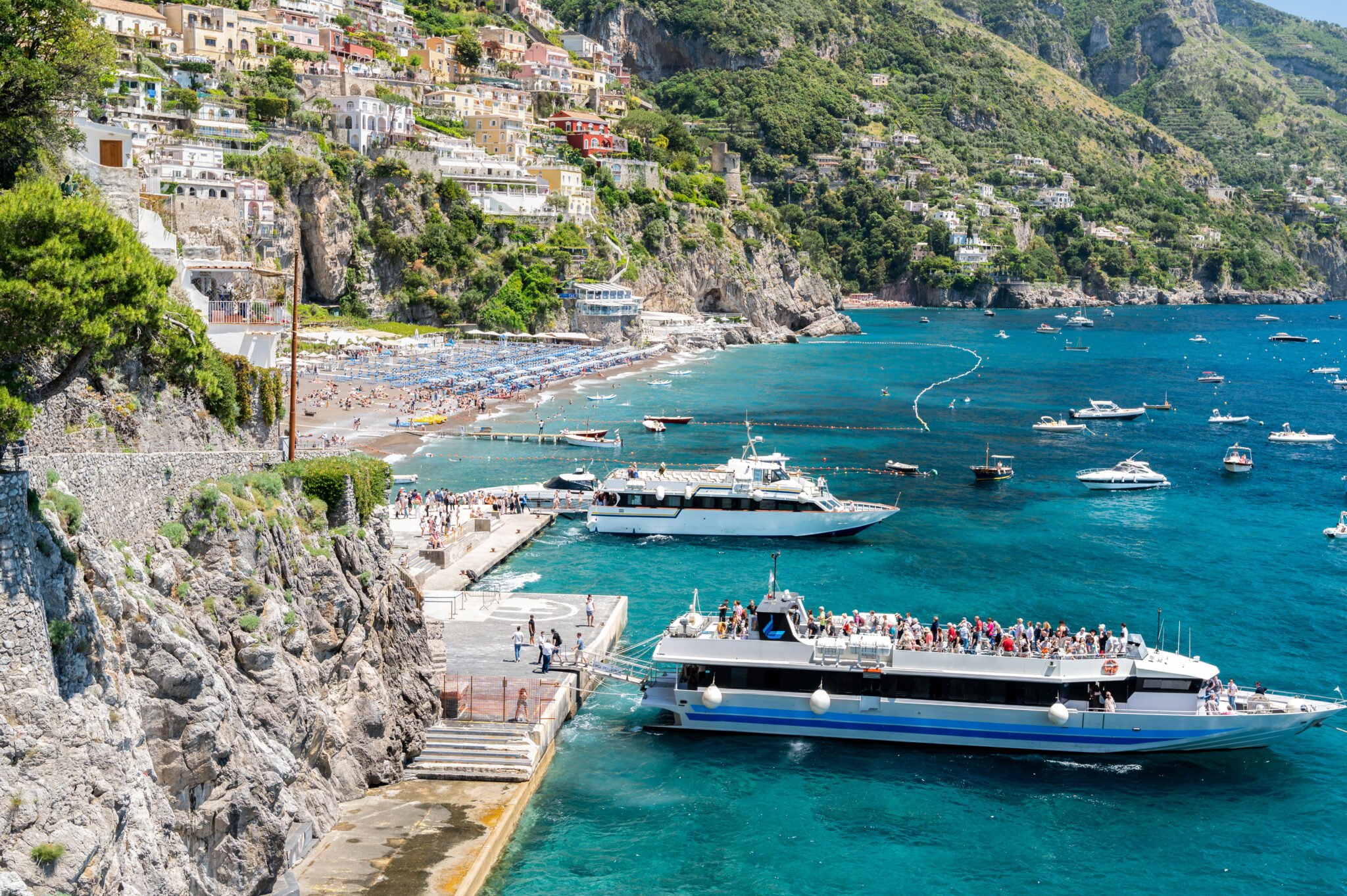 Positano ferry dock and beach promenade with boats in the bay.
